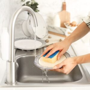 person washing dishes in kitchen sink