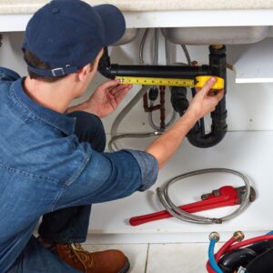 plumber measuring pipes under sink