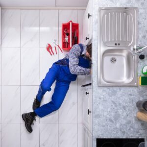 plumber on the floor working on the drains under a sink 