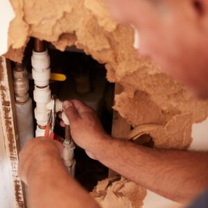 plumber works on pipes in the wall 