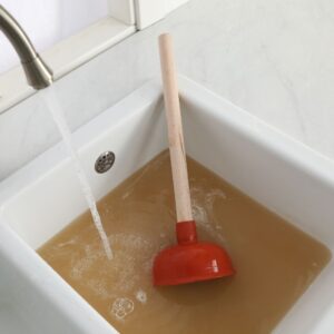 sink full of dirty water with a plunger to unclog drain 