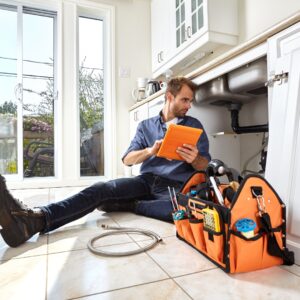 plumber sits underneath kitchen sink with tools 