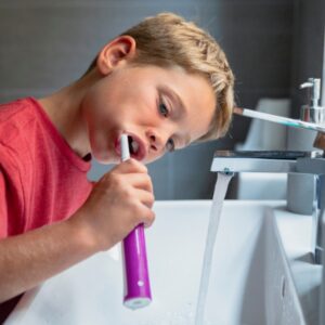 Boy brushing his teeth with faucet running