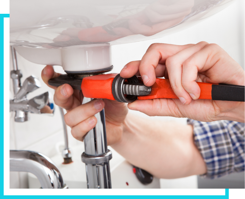 Close-up of a plumber using a pipe wrench to repair a commercial sink fixture and drain assembly.