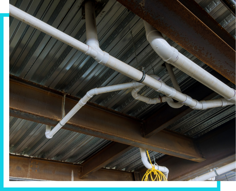 Overhead view of commercial plumbing rough-in featuring PVC waste lines and venting installed along a steel building frame.