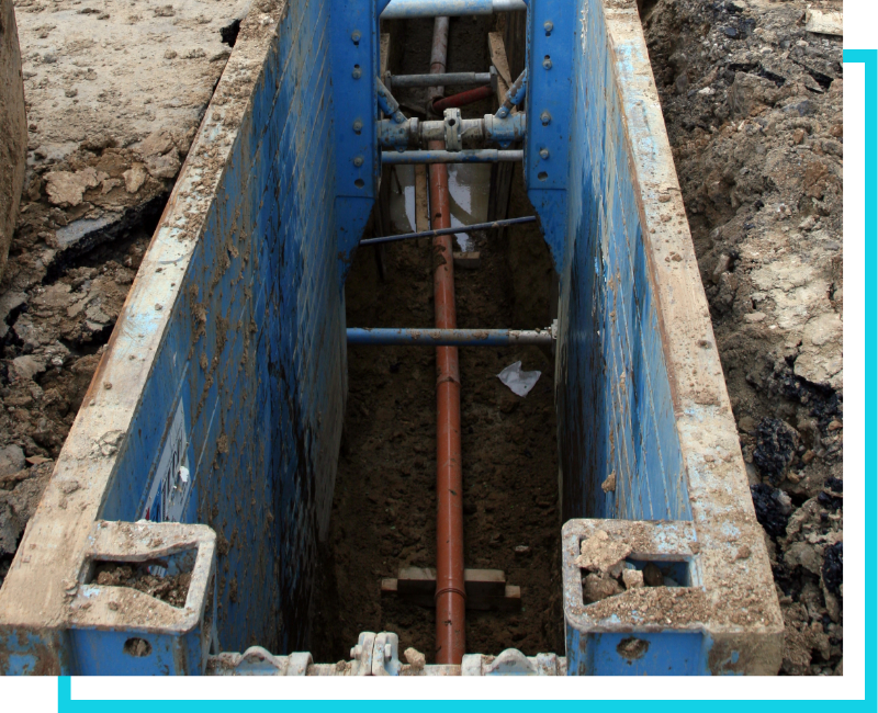 Deep trench excavation for a commercial sewer hookup featuring blue trench shoring and main line piping.