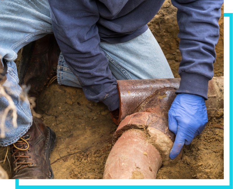 Technician in blue gloves inspecting a large cast-iron water main junction in an excavated trench for commercial repair.