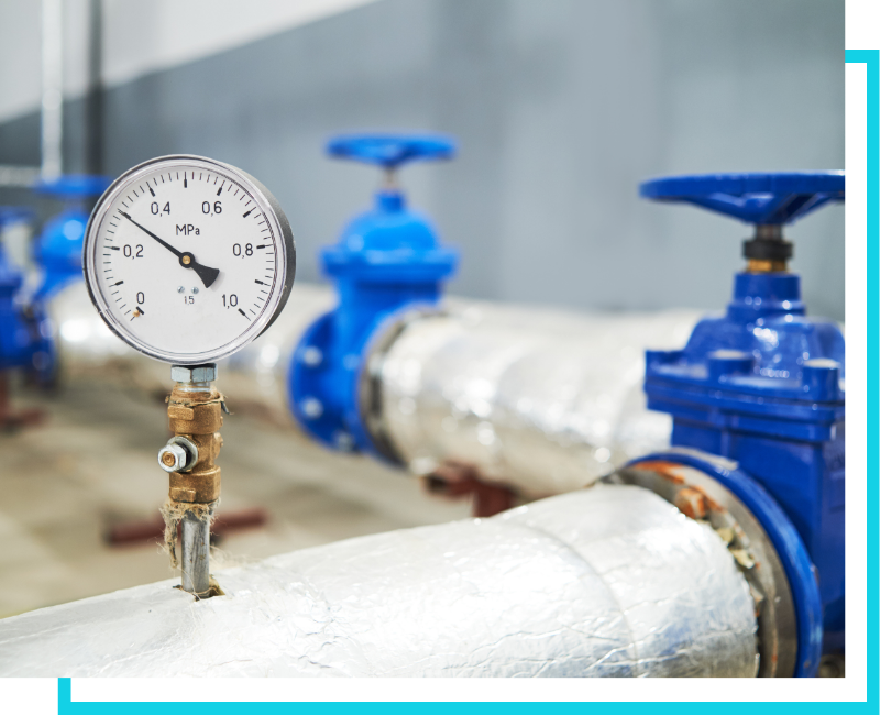 Close-up of a pressure gauge and blue shut-off valves on an insulated commercial water distribution system.